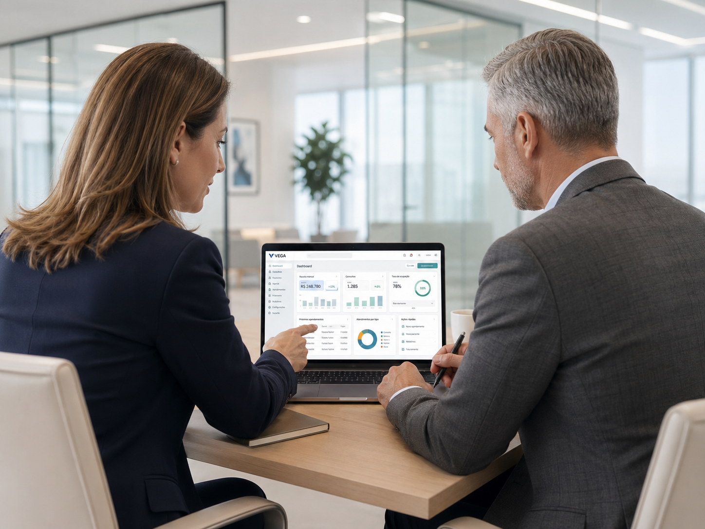 Conversa consultiva em torno do VEGA em um ambiente executivo premium, com o notebook naturalmente visível entre os dois profissionais.